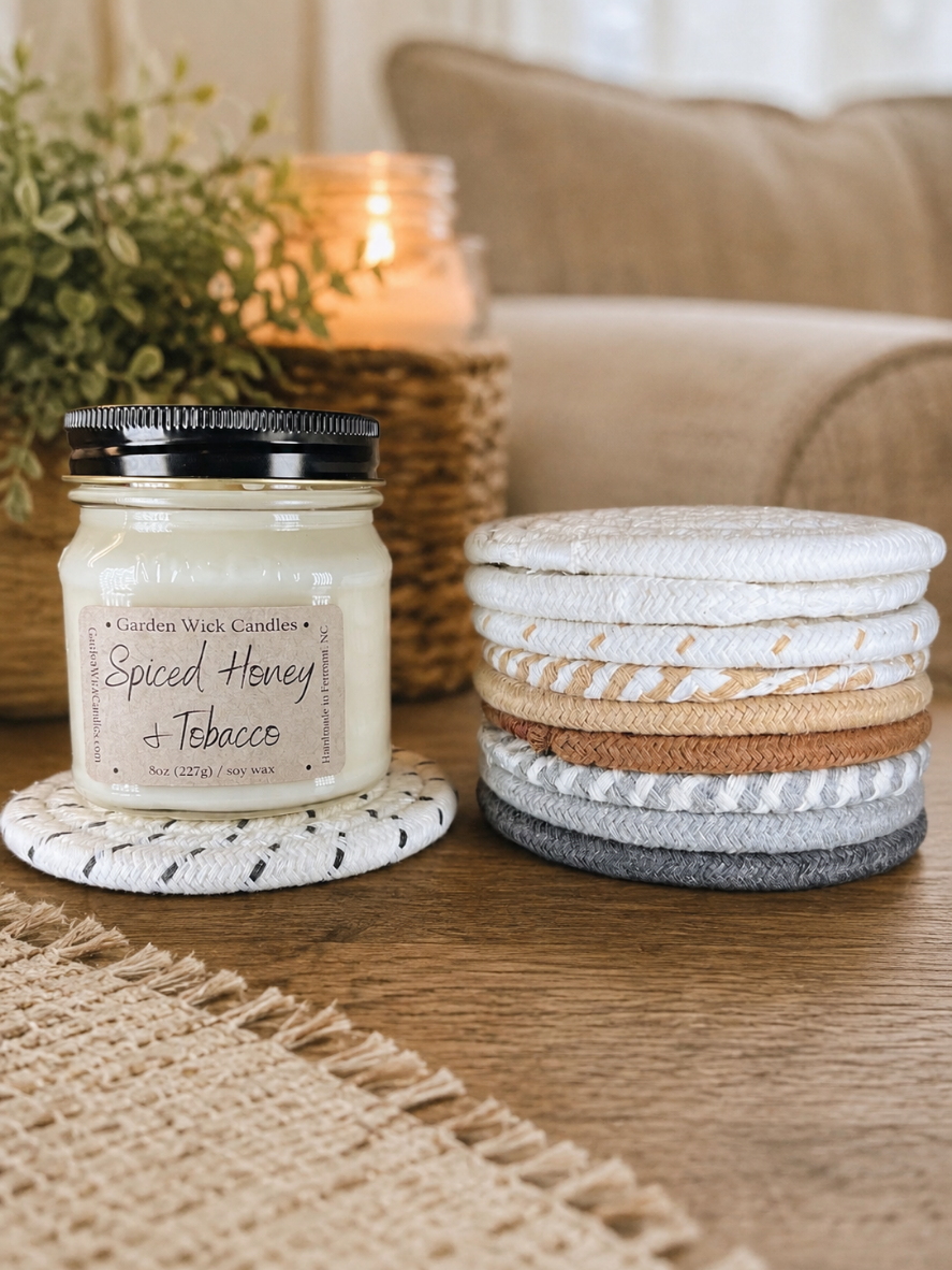 garden wick candle on a woven candle coaster beside a stack of neutral candle coasters in a cozy home setting.
