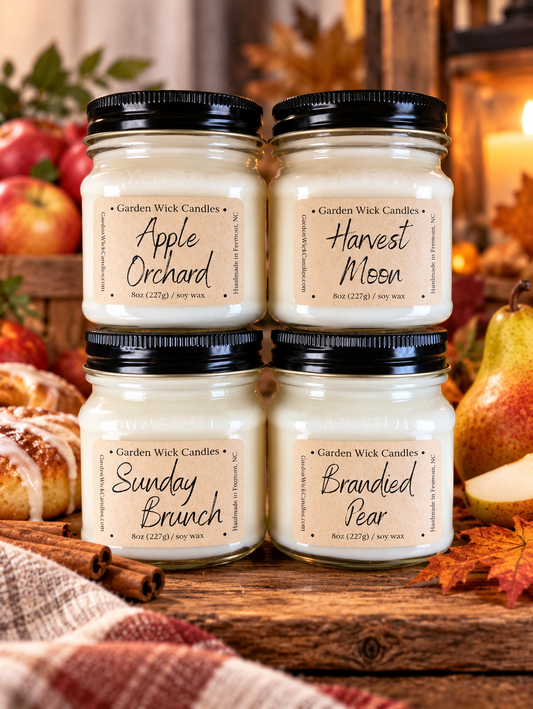 Four glass jar candles from Garden Wick Candles arranged in a 2x2 grid on a rustic wooden surface. The jars contain creamy off-white wax and have black screw-on lids, with labels for Apple Orchard, Harvest Moon, Sunday Brunch, and Branded Pear. Garden Wick Gathering Season Bundle with four 8 oz soy candles in Apple Orchard, Harvest Moon, Sunday Brunch, and Brandied Pear.
