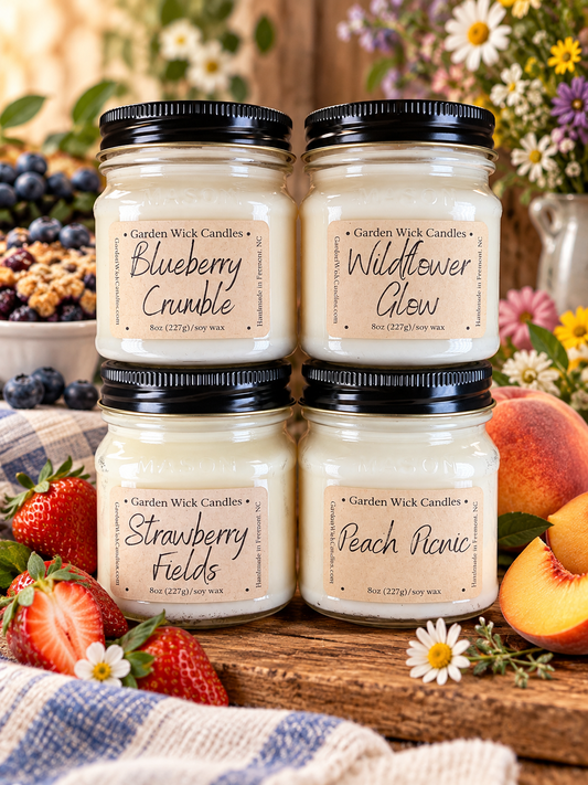 Four Garden Wick Candles in clear glass jars with black lids, arranged on a wooden surface with strawberries, peaches, flowers, and a plaid cloth. The labels read Blueberry Crumble, Wildflower Glow, Strawberry Fields, and Peach Picnic. Garden Wick Sugar & Sunshine Bundle with four 8 oz soy candles in Blueberry Crumble, Wildflower Glow, Strawberry Fields, and Peach Picnic